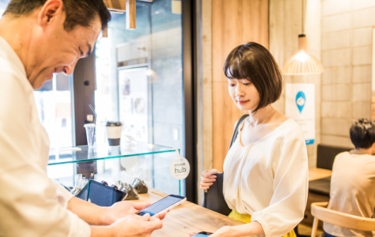 Man scanning a barcode on a woman's phone inside a store at the counter.