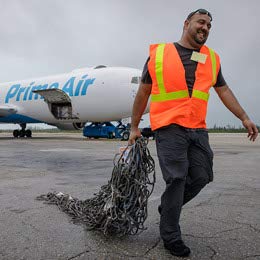 A man carries netting across a tarmac with a plane in the background.