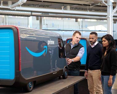 Three people look at a scale model of a delivery van.