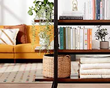 Living room image with bookcase used as a room divider. Caption reads small space solutions. Shop furniture & more