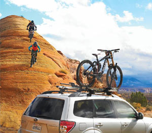 Mountain bikers riding toward a Thule Sidearm Rooftop Upright Bike Carrier mounted on an SUV
