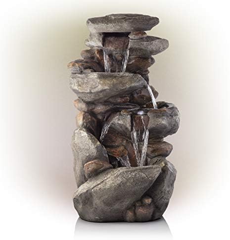 Tiered water fountain with intricate design, placed in a backyard setting near double doors.