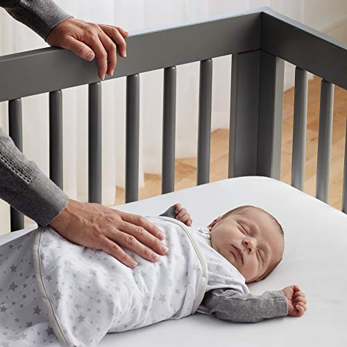 A child sleeping in a cotton baby wrap carrier on a person's hip.