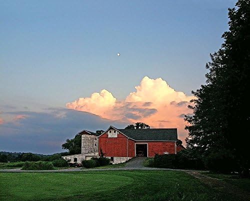 Red Barn At Sunset. A fine art photograph of a large red barn with thunderheads piled behind it in an evening sky with the moon. Peaceful yet dramatic.