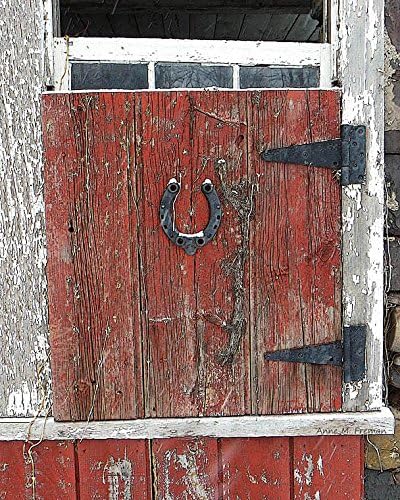 Boarded Barn Window with Horseshoe. Photograph of an old barn window is boarded shut by a handmade red plank shutter with an old iron horse shoe. It has just started snowing.