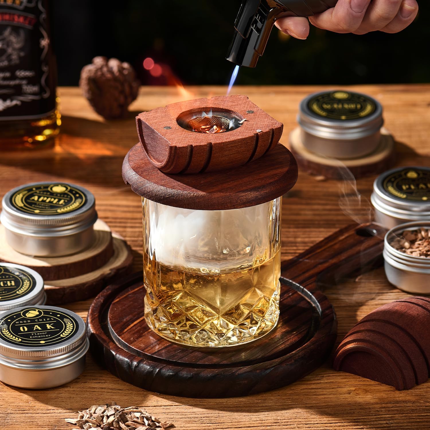 whiskey smoker lid resting on a filled rocks glass on a dark wood table with smoke curling out and wood chip tins beside it