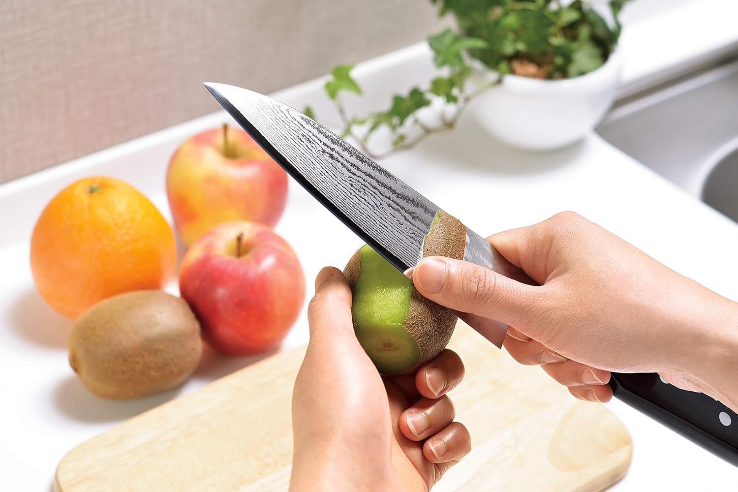 まな板や果物が置かれたシンクの上でキウイの皮をむいている様子