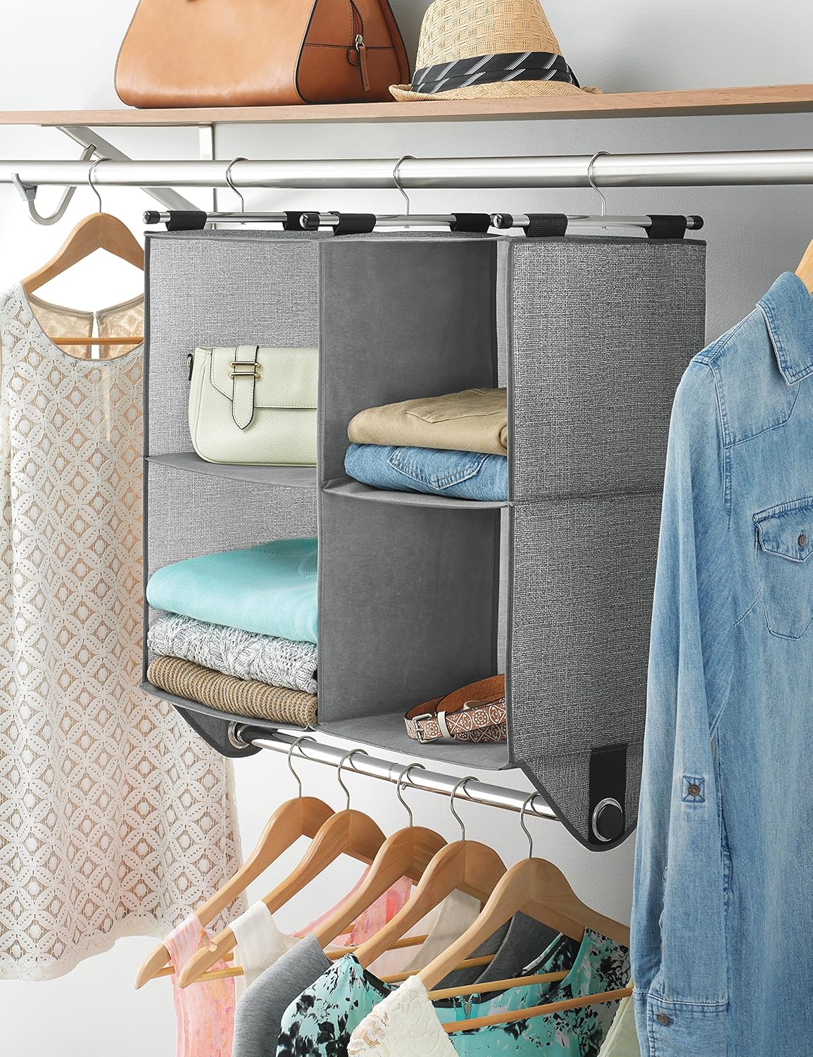 A four cube closet organizer hanging on a silver rod amongst varying clothes and accessories. 