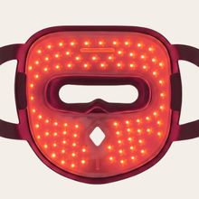 Máscara facial de terapia com luz LED vermelha com design de superfície perfurada, alças de tecido ajustáveis e pequenos detalhes decorativos em forma de diamante na parte frontal.
