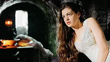 Anne Hathaway as Ella standing in a medieval marketplace with Hugh Dancy as Prince Char in the Ella Enchanted game.