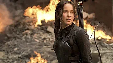 Jennifer Lawrence as Katniss Everdeen standing in the ruins of District 12 in the poster for The Hunger Games: Mockingjay Part 1 game.